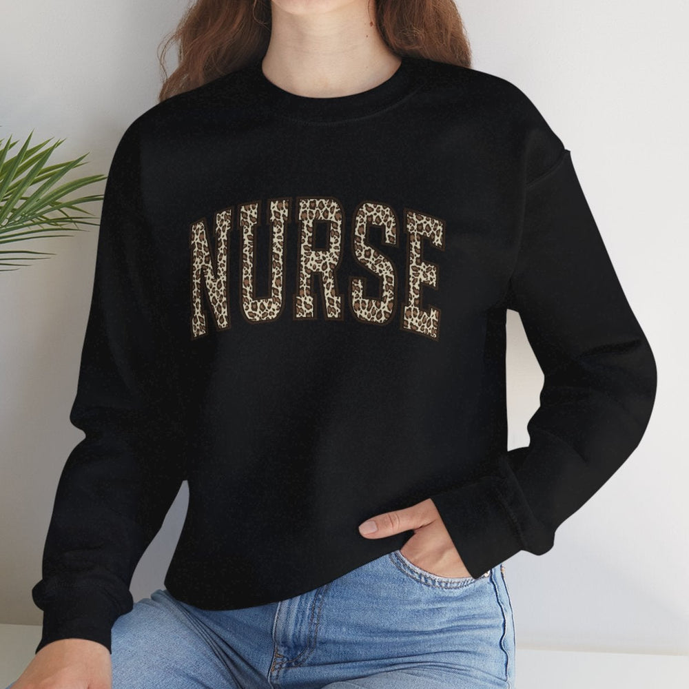 Woman wearing a black 'NURSE' sweatshirt sitting on a white surface with a plant in the background.